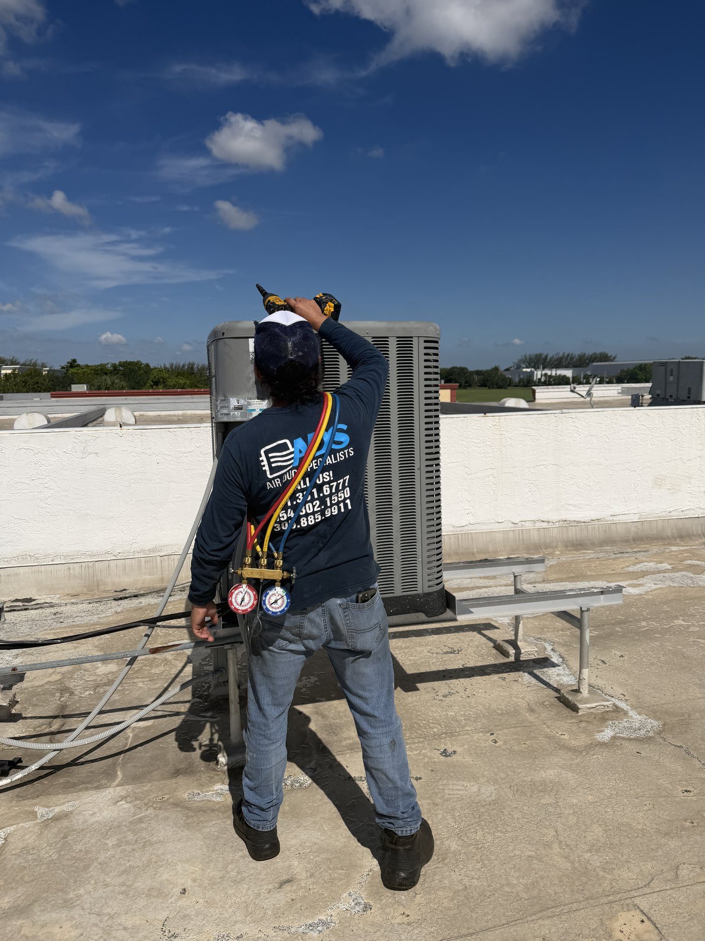 Air Duct Specialists LLC technician with refrigerant manifold gauges on a rooftop condenser during preventive AC maintenance in South Florida