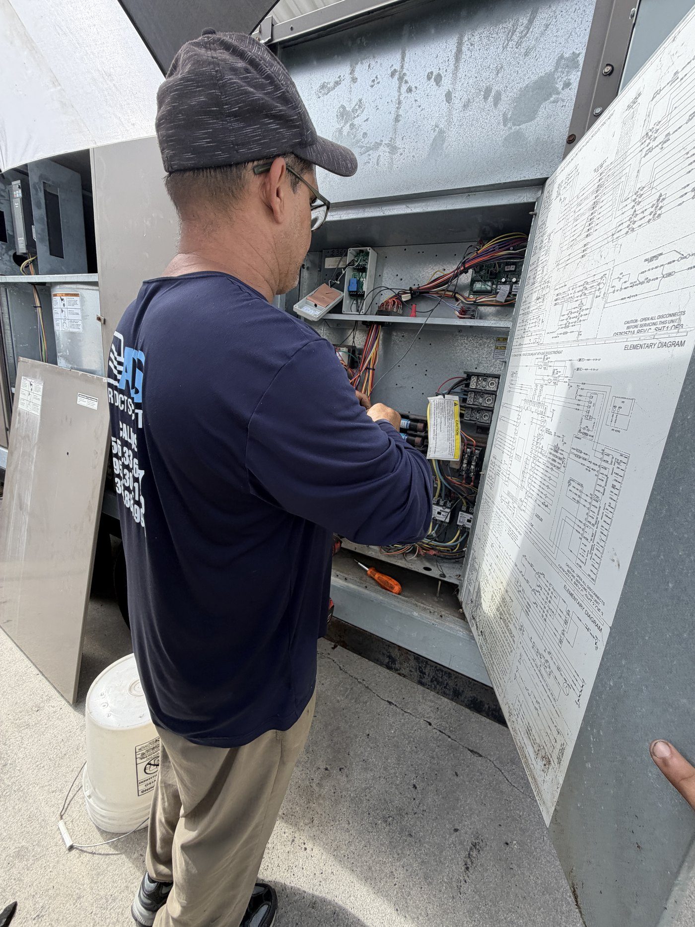 Air Duct Specialists LLC technician tracing control wiring against the elementary diagram during an AC repair diagnostic in South Florida