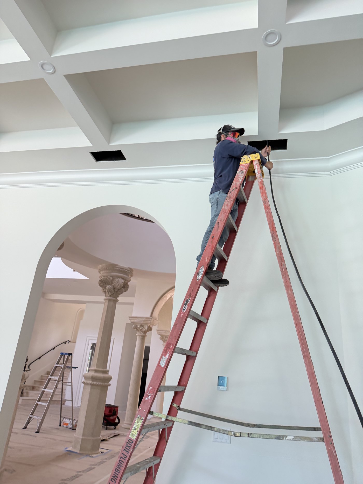 Air Duct Specialists LLC technician on a ladder cleaning a supply register in a coffered ceiling of a Boca Raton estate home