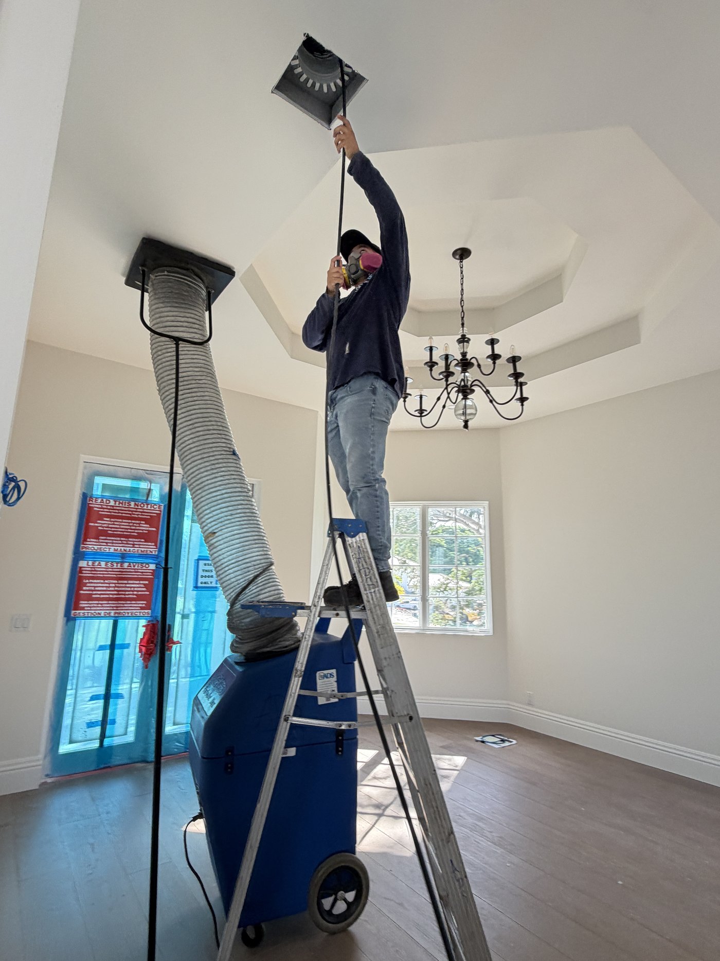 Air Duct Specialists LLC technician cleaning a ceiling supply register with a negative air machine running in a Boca Raton estate home
