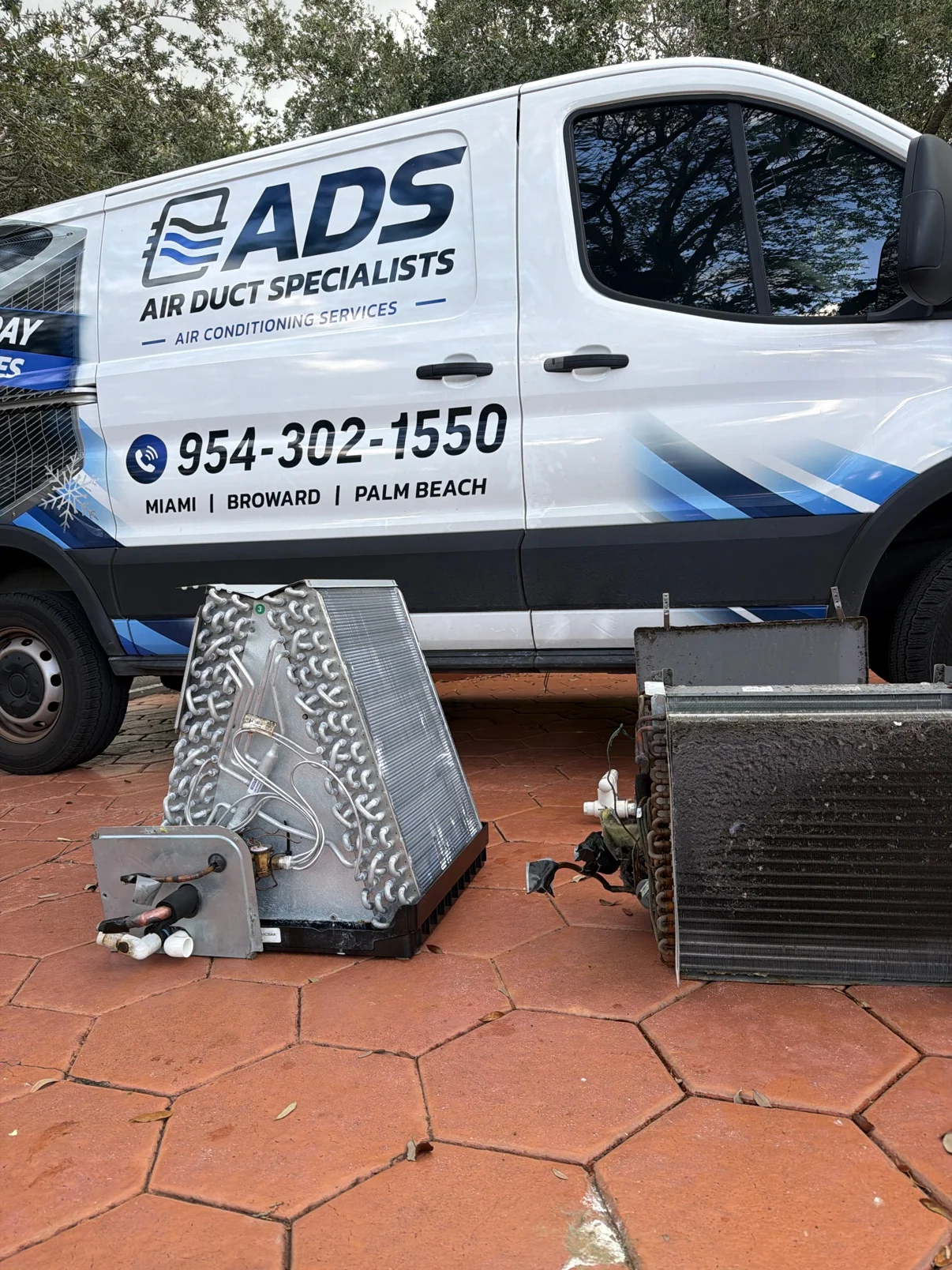 Two removed evaporator coils in front of an ADS van, one cleaned and one still dirty with buildup — Air Duct Specialists LLC