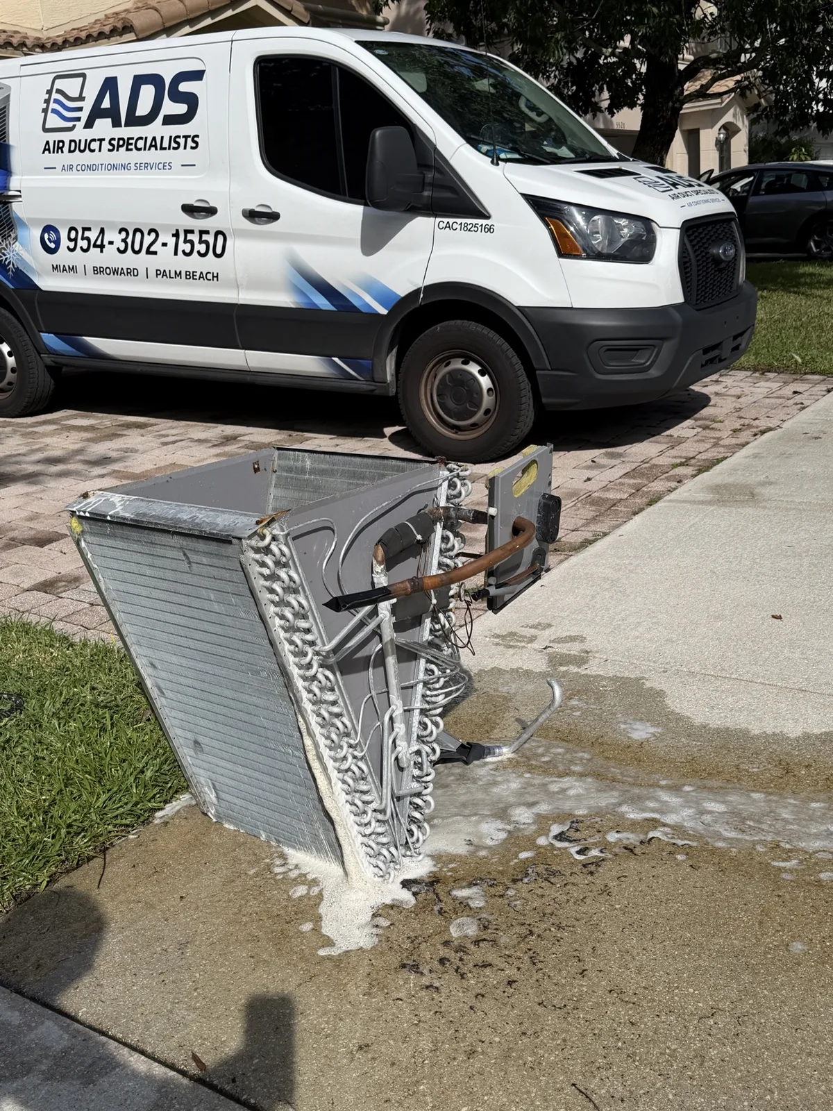 Removed evaporator coil covered in foaming cleaner in front of an Air Duct Specialists van — Air Duct Specialists LLC