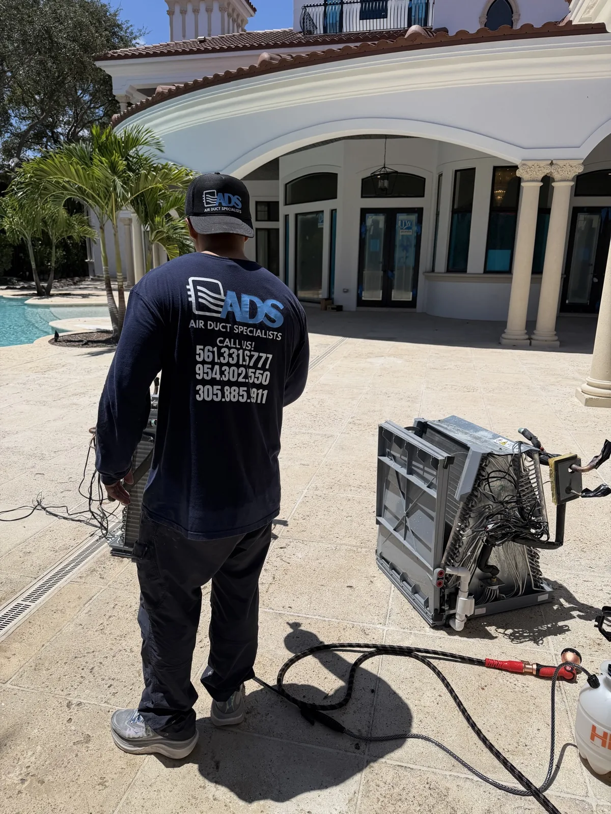 Air Duct Specialists technician beside a removed evaporator coil on a luxury home's pool patio