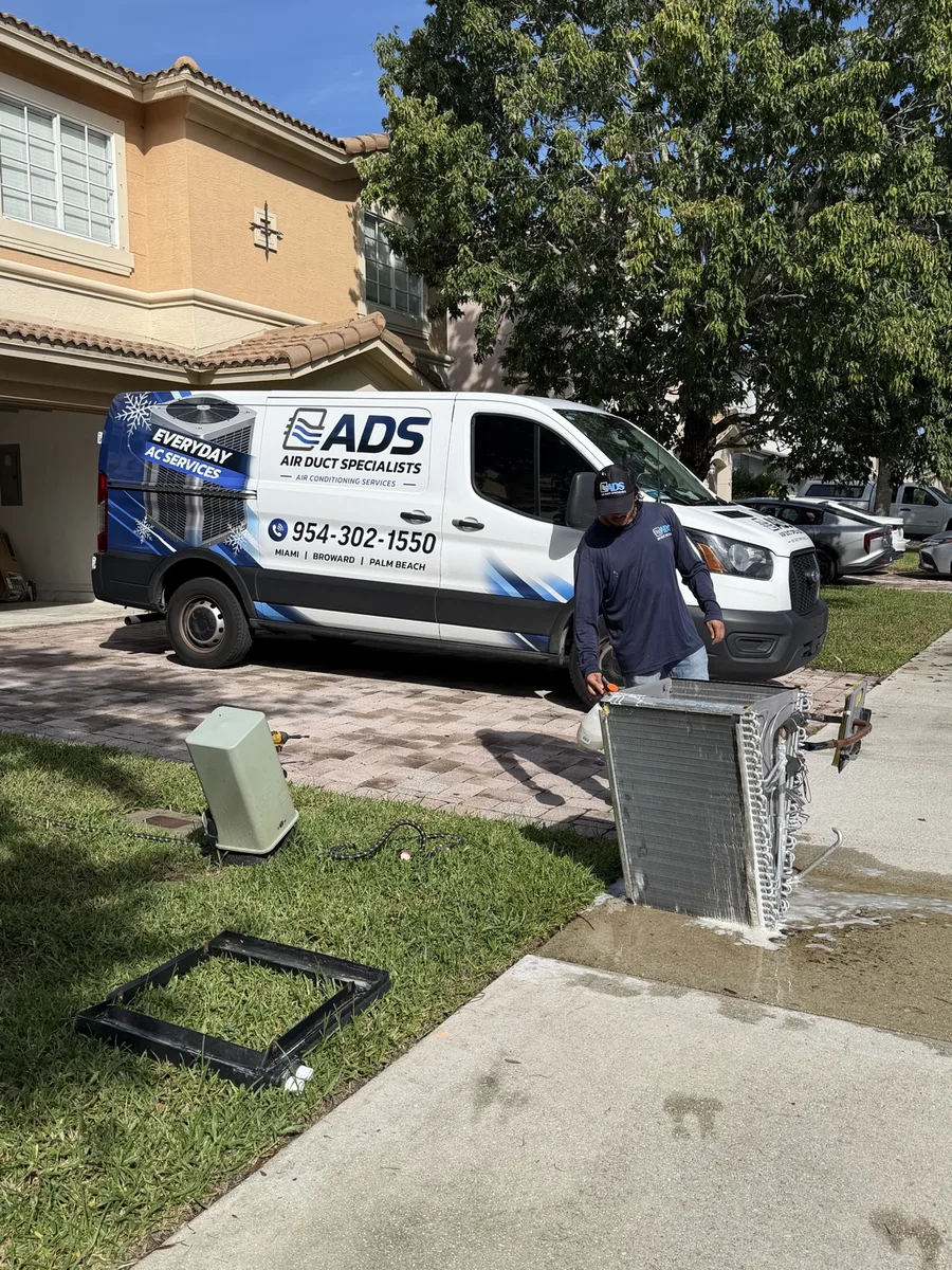 Air Duct Specialists technician applying professional cleaner to a removed evaporator coil in front of the service van — Air Duct Specialists LLC