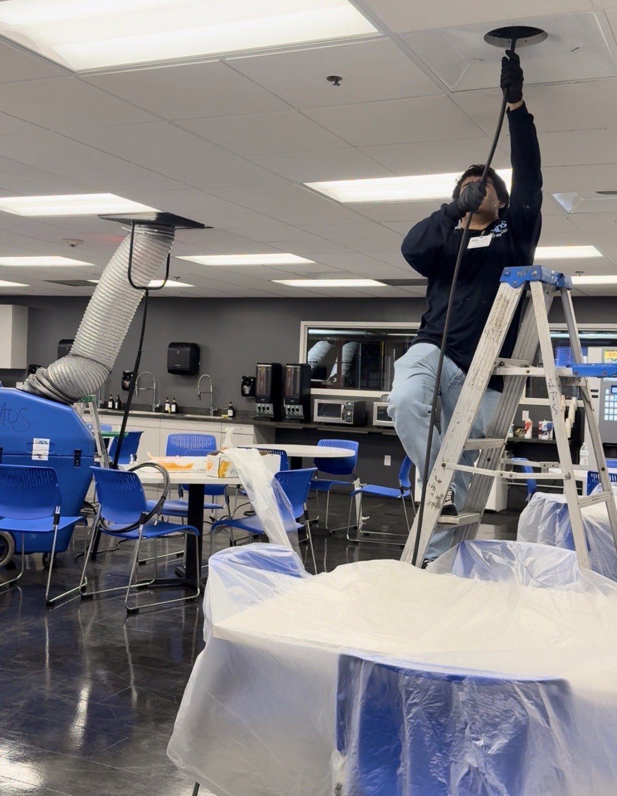 Air Duct Specialists technician cleaning ceiling supply ducts in a commercial breakroom with negative air containment in South Florida