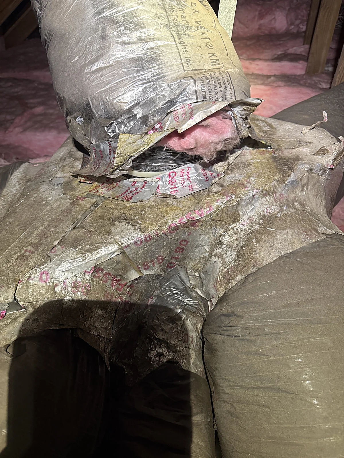 Torn flexible duct with exposed pink fiberglass insulation and a loose connection in a Coral Gables attic