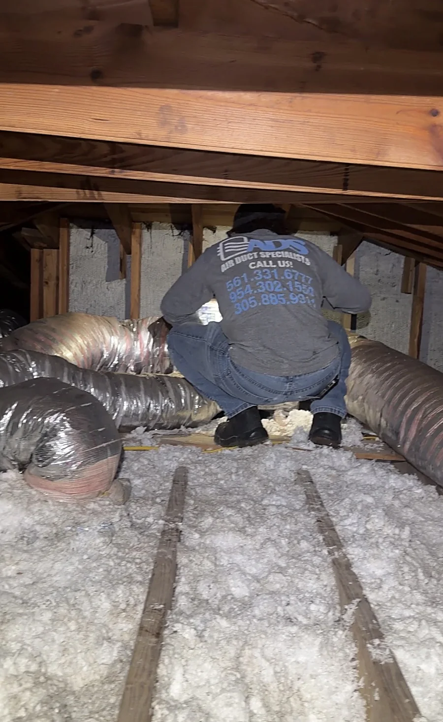 A technician in a South Florida attic assessing old ductwork that is scheduled for replacement