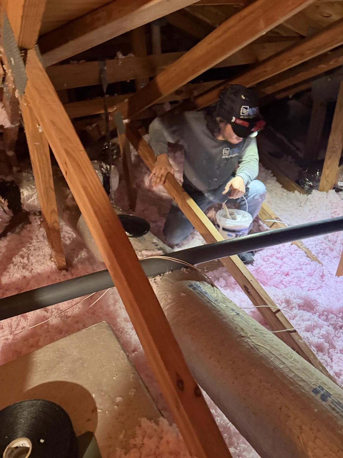 A technician sealing duct connections by hand with mastic in a South Florida attic — Air Duct Specialists LLC