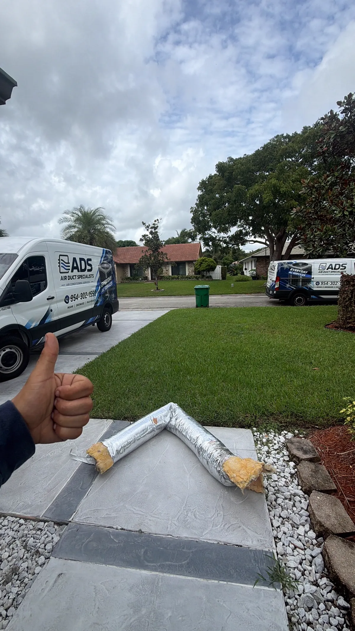 An old flex duct run removed and laid out in front of a South Florida home with two service vans — Air Duct Specialists LLC