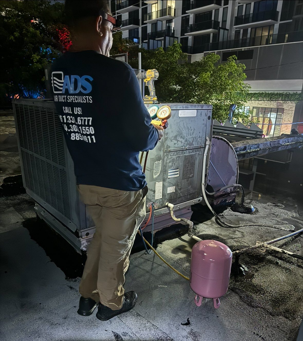 Air Duct Specialists technician gauging up a rooftop package unit on a night emergency AC repair call in South Florida