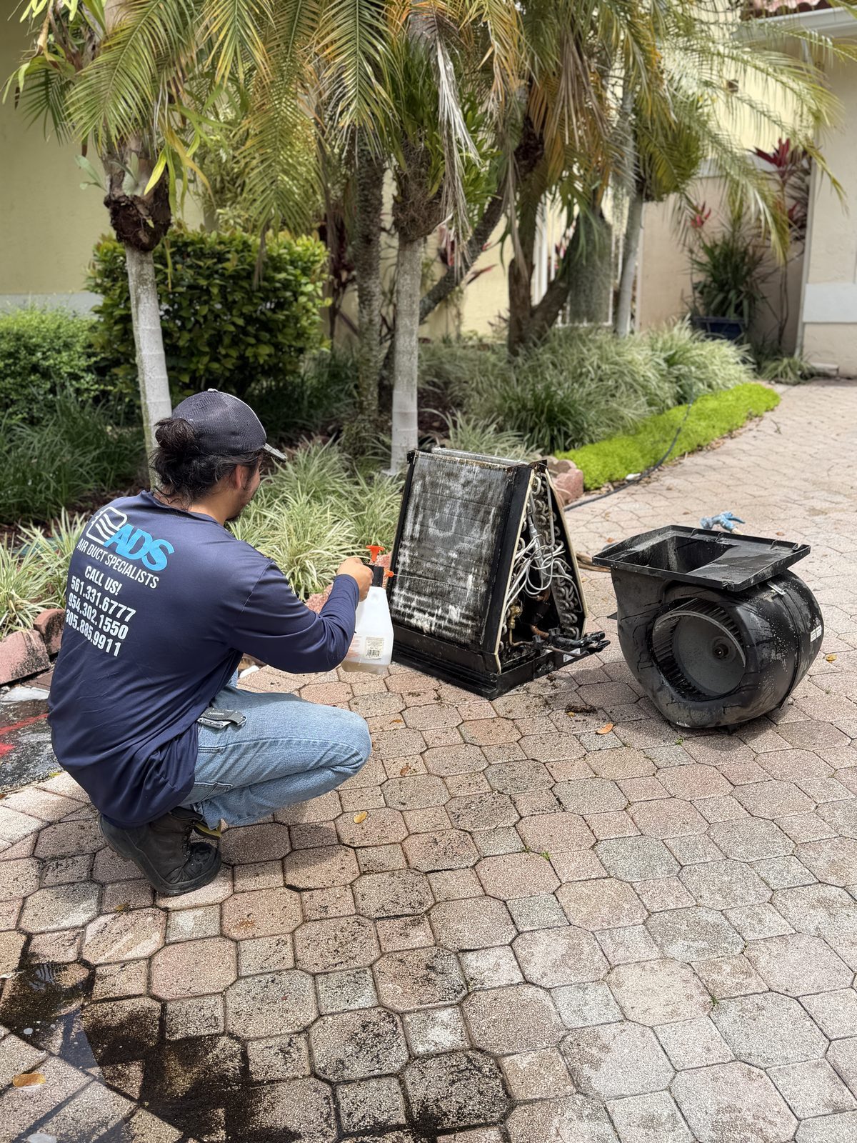 Technician cleaning a blower motor assembly and coil removed from a South Florida air handler