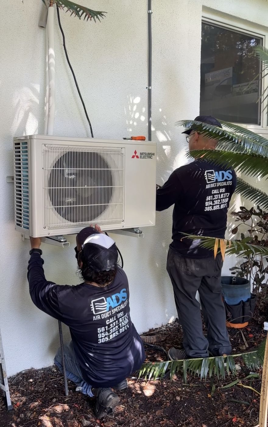 Air Duct Specialists crew mounting a Mitsubishi ductless mini split condenser on a South Florida home